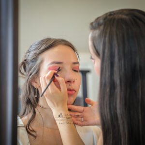 Makeup artist applying eyeshadow to bride before wedding ceremony.