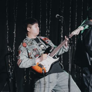 Musician in denim jacket playing electric guitar energetically on stage