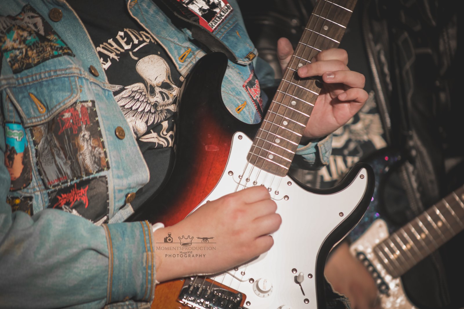 Musician in denim jacket strumming electric guitar on stage.