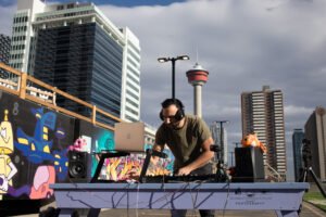 DJ mixing music on rooftop with Calgary Tower and downtown buildings in the background.