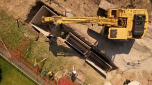 Drone photo of yellow excavator digging and placing concrete structures at a construction site.