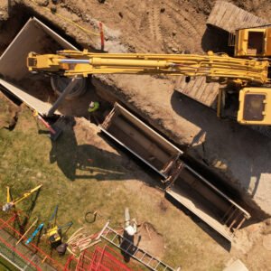 Drone photo of yellow excavator digging and placing concrete structures at a construction site.