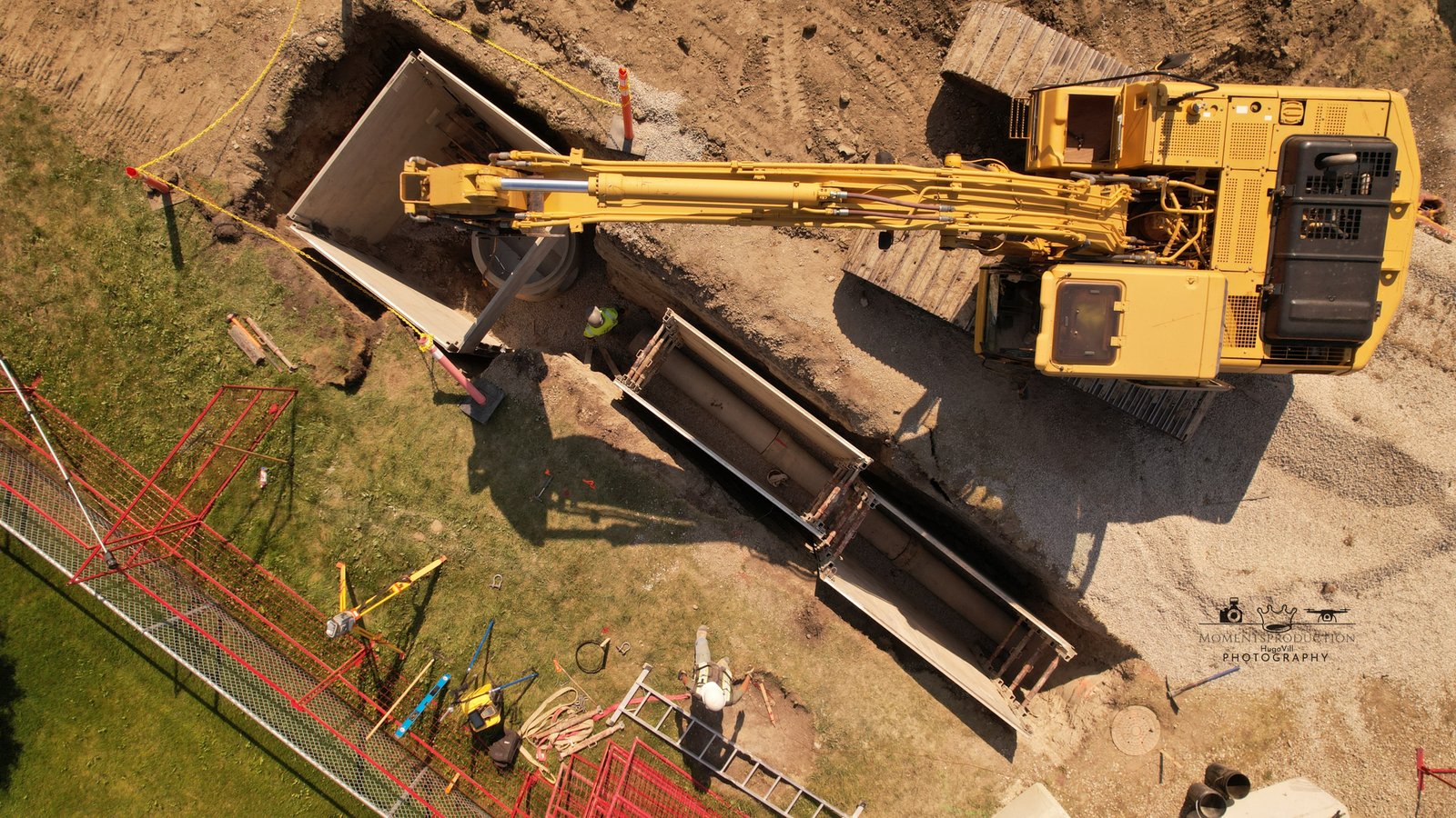 Drone photo of yellow excavator digging and placing concrete structures at a construction site.